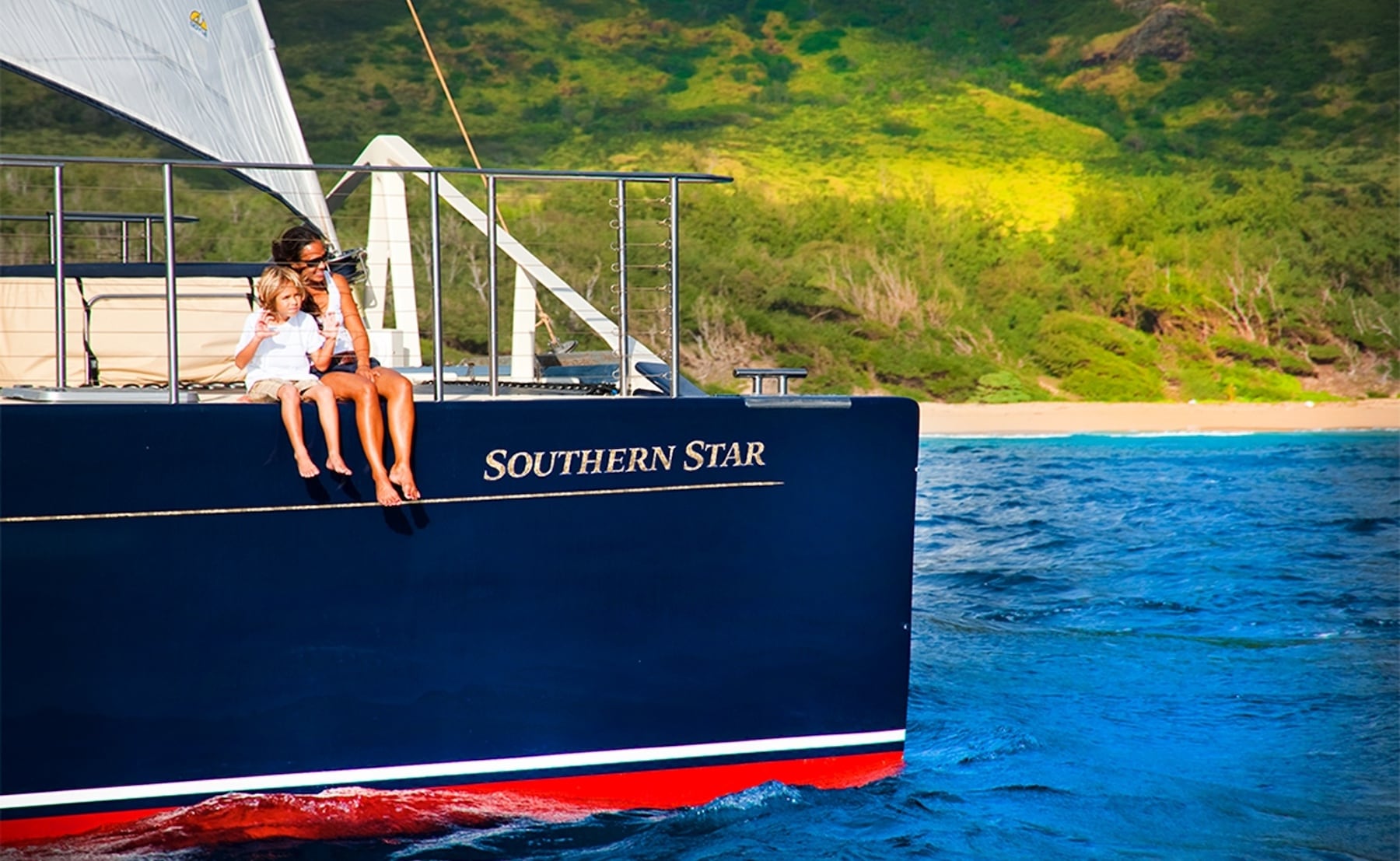 A mother and child sit on the deck of the Southern Star catamaran, enjoying a Na Pali Coast sunset tour.