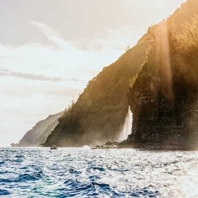 Sunlight streaming over the dramatic cliffs on a Na Pali boat tour Kauai.