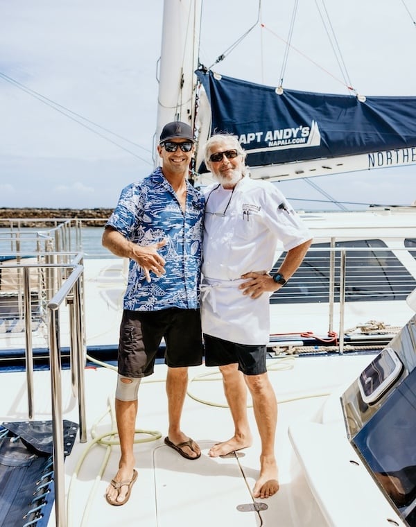 Captain Andy's crew is on a Star Yacht. One crew member is wearing a blue Hawaiian shirt throwing a shaka sign, and the other is in a white chef uniform.