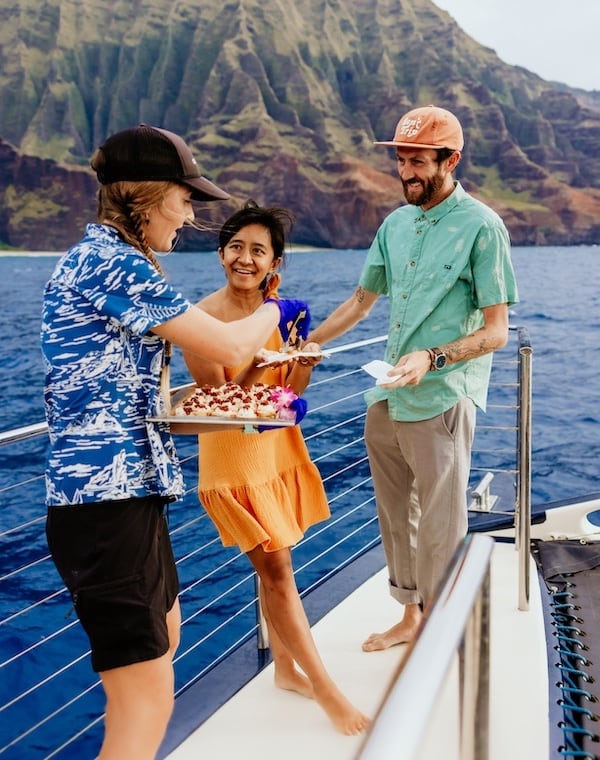 Captain Andy's crew member serving food to smiling guests on a boat near the Na Pali Coast