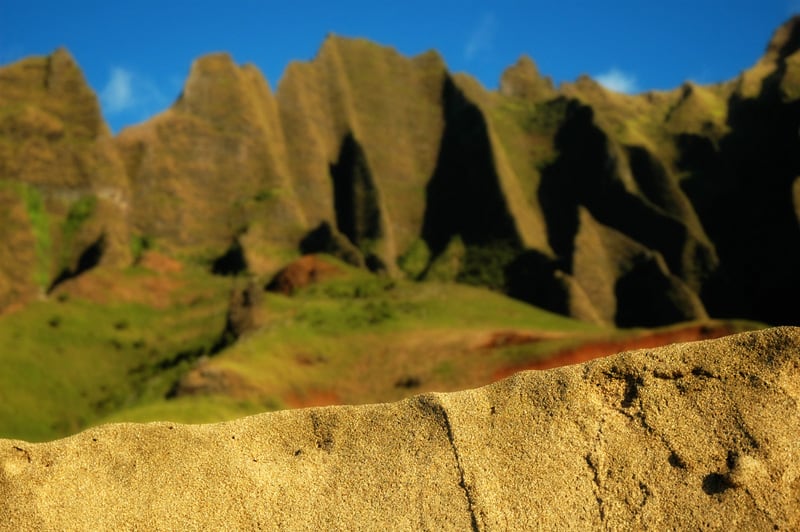 The iconic green and red cliffs of the Na Pali Coast in the blurred background under a bright blue sky.