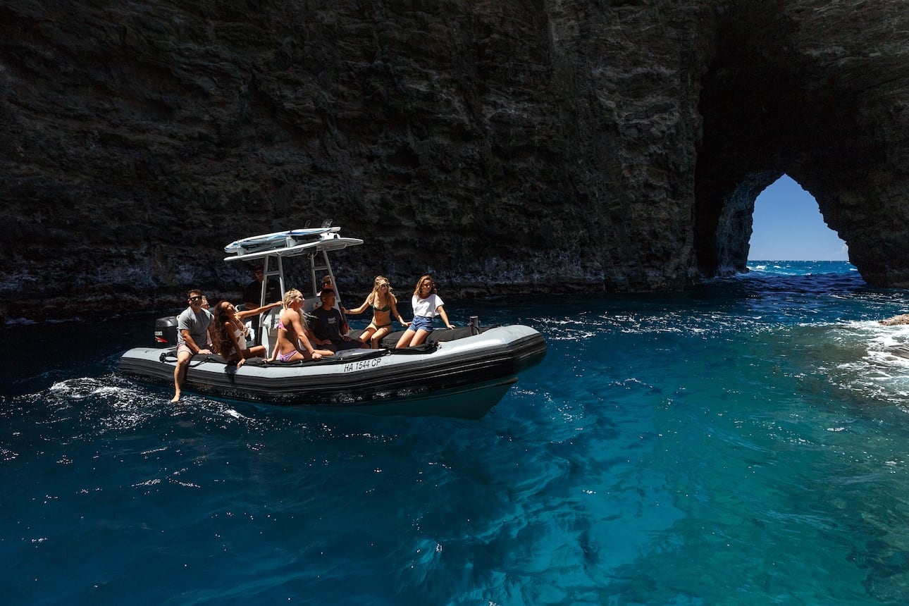 Boat navigating with passengers through a rocky archway along the Na Pali Coast.